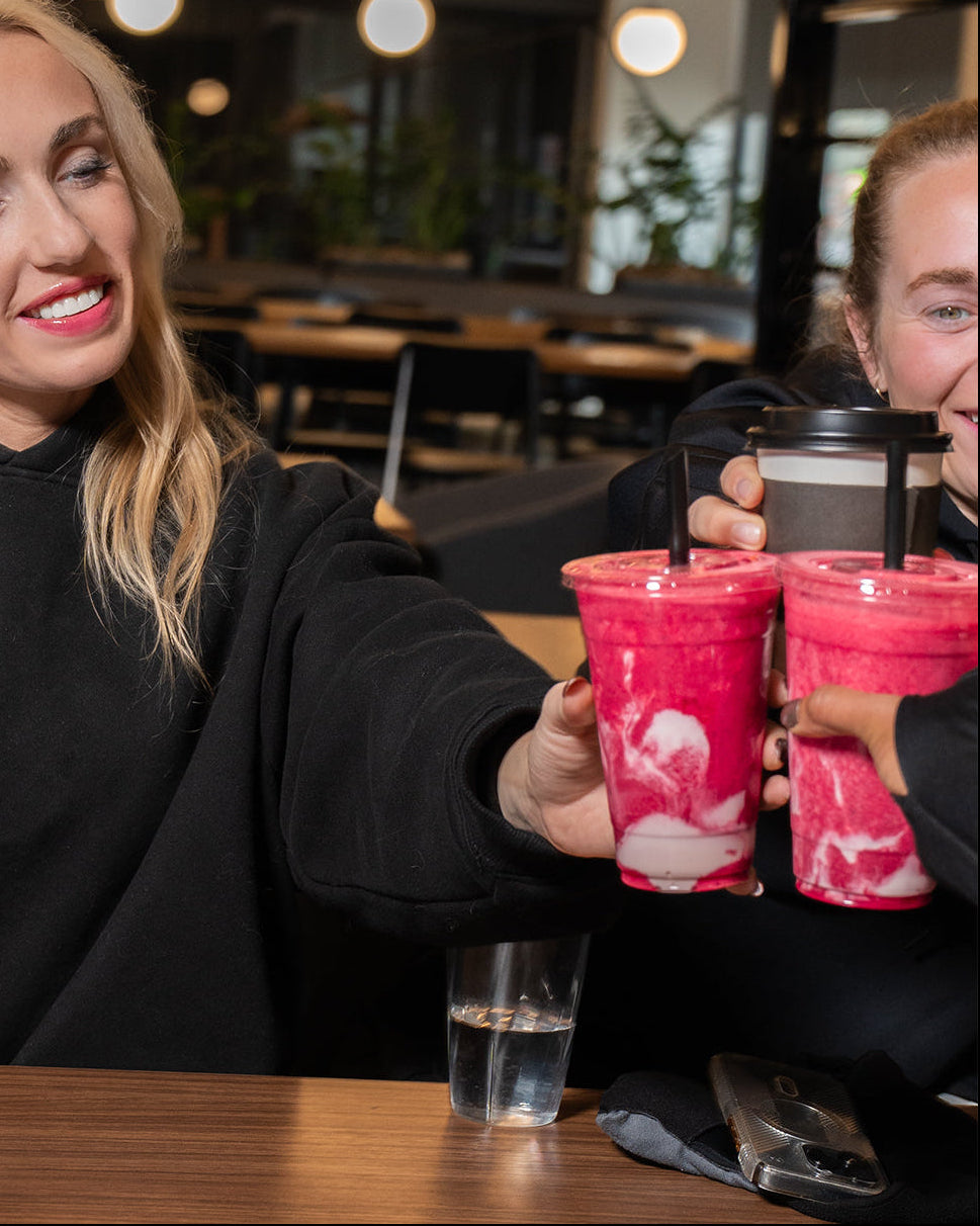 Two women holding pink smoothies with straws in a casual setting